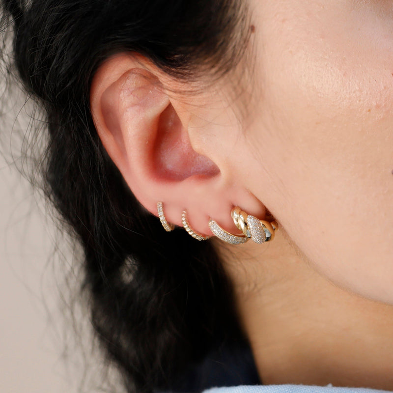 Model wears four piercings featuring thick croissant twist ear huggie in solid 14k gold. 