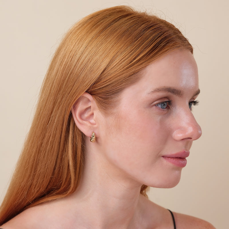 Model wears handcrafted solid 14k gold thick huggie earring in twisted croissant design.