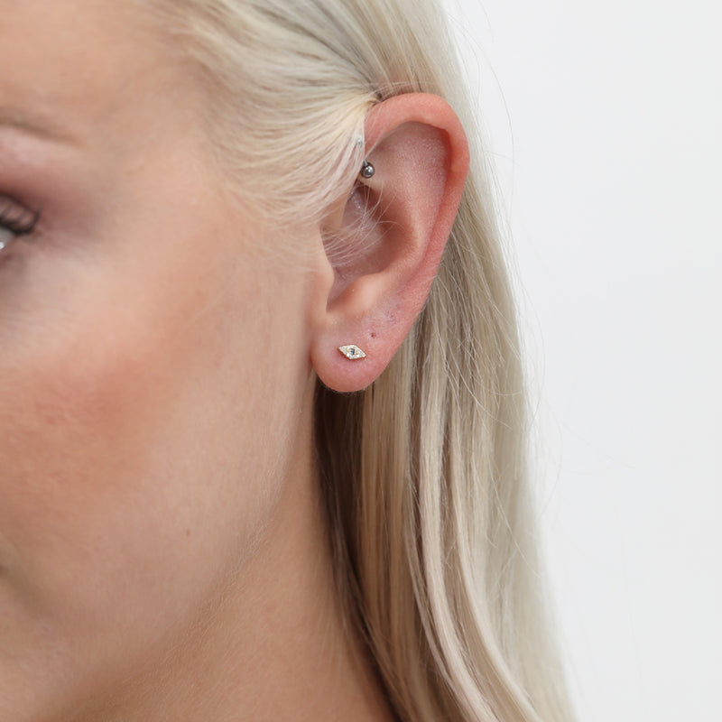 Model wears evil eye stud earring with paved diamonds and single blue sapphire