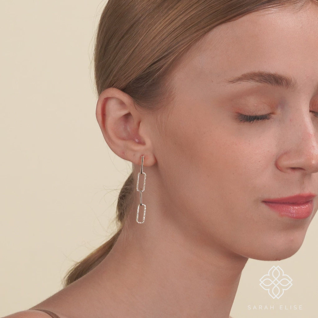 Video of model wearing drop down chain link stud earrings lined in white diamonds