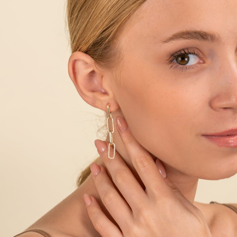 Model wears hanging chain link stud earrings lined in white diamonds