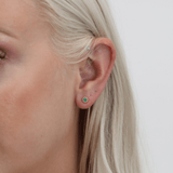 Model wears dainty May birthstone emerald stud earrings in 14k solid gold