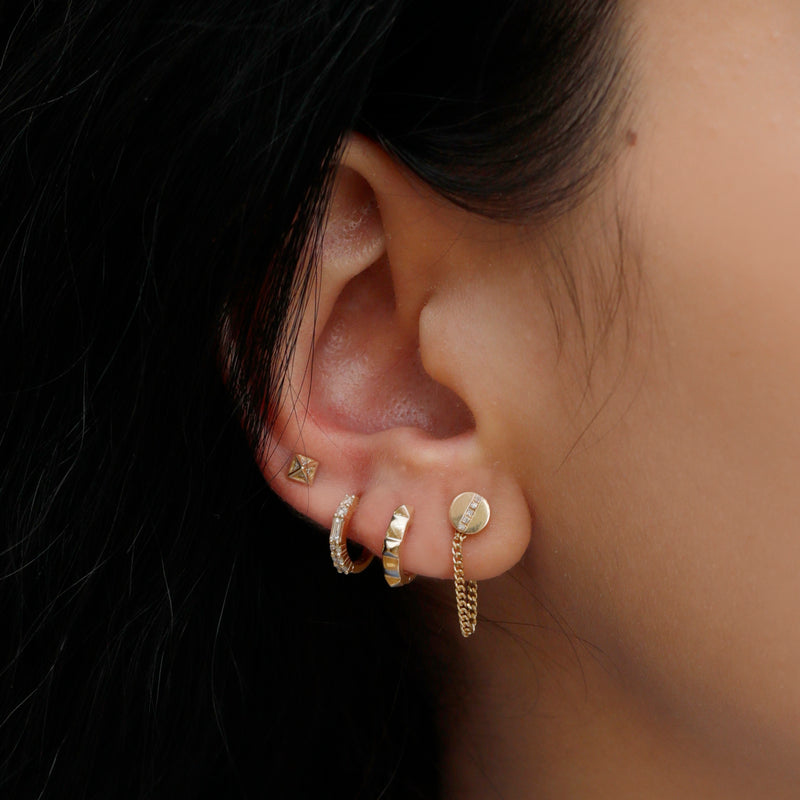 Model wears multiple piercings featuring solid 14k gold handcrafted pyramid spike round ear huggie. 