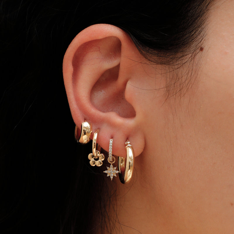 Model wears 4 earring hoop stack featuring handmade solid 14k gold flower charm hoop earring. 