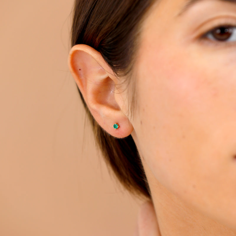 Model wearing dainty emerald May birthstone studs in 14k solid gold.