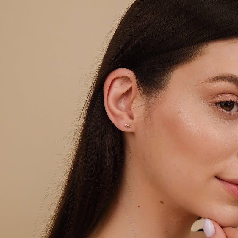 Model wearing minimalistic Solid gold infinity symbol stud earring.