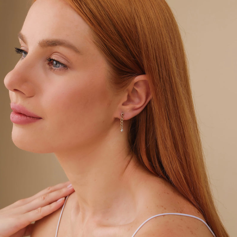 Model wears dainty ethically sourced fine jewelry stud earrings with hanging cuban chain and single natural diamond april birthstone gift for her