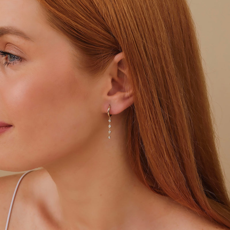 Model wears handmade solid gold huggie earrings with hanging four bezel diamonds