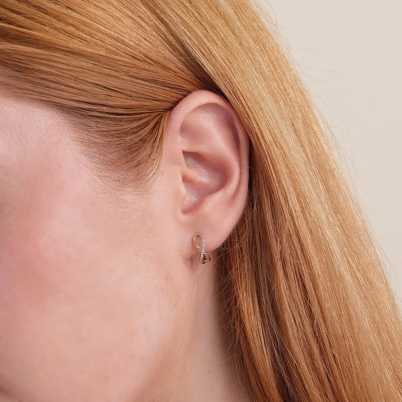 Model close up wearing dainty curved infinity symbol April birthstone earrings.