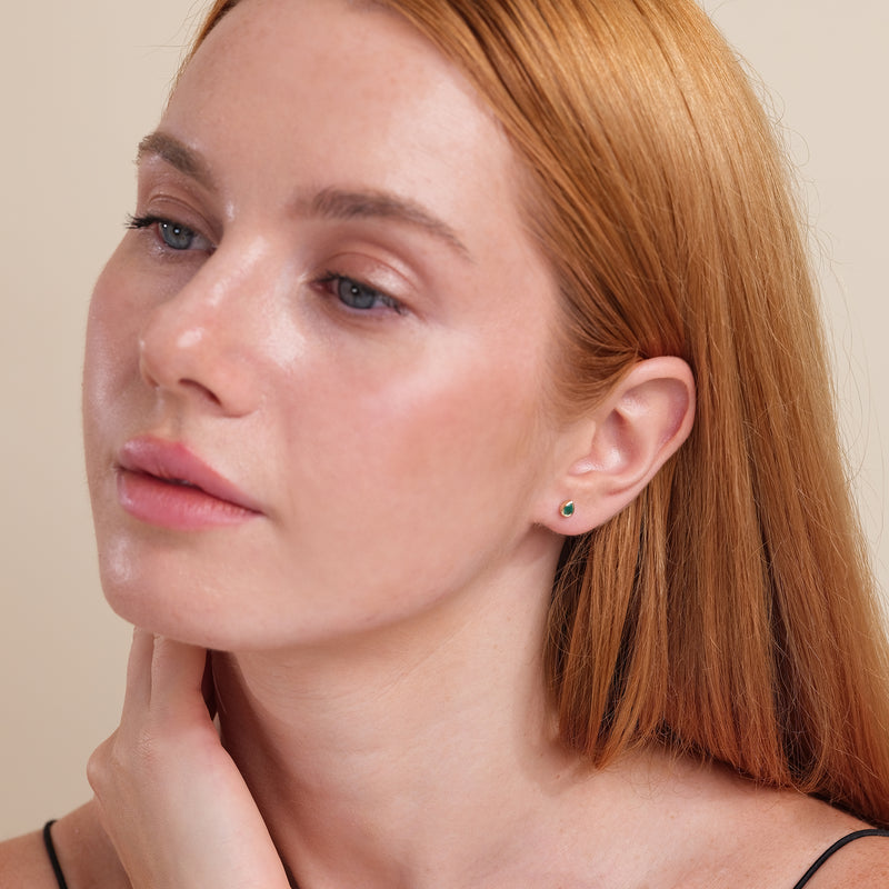Model wears single dainty pear cut emerald stud earring in 14k solid gold.
