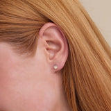 Model image close up wearing petite solid gold dog paw shaped earring studs with natural April birthstone diamonds. 