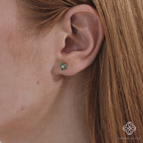 Video close up of model wearing flower diamond stud with dainty green natural emerald stones in solid 14k gold. 
